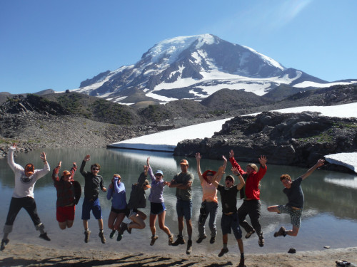 Image shows: a group of people jumping in the air with a view of Mt Adams behind them.