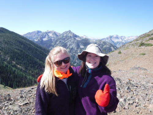 Image shows two students smiling, standing in front of a view of the Wallowa Mountains
