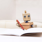 Image of a cardboard robot writing in a notebook with a pen
