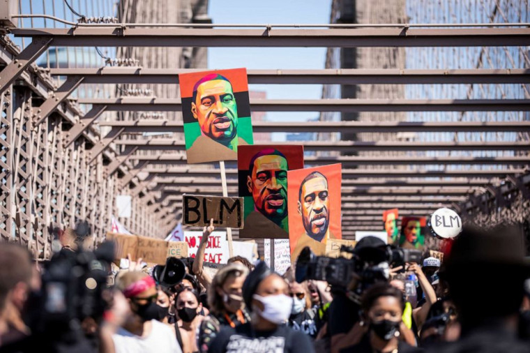 Thousands of protesters walk in a peaceful protest across the Brooklyn Bridge holding signs that read, BLM and three painted portraits of...