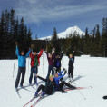 A group of participants pose in front of Mt. Hood wearing cross-country skis with their hands in the air smiling.