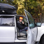 Image shows a man in an orange hat and black jacket sitting in a white vehicle. The door is open ...