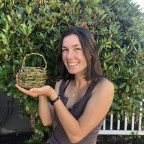 Woman holds up a basket she made from natural materials