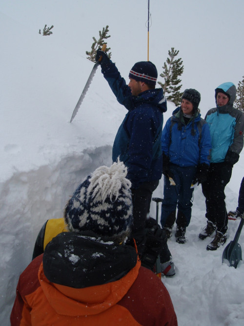 An instructor cuts into the snow to remove a block of ice for analysis.