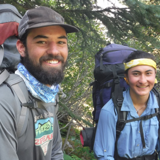 Image Description: Two men wearing backpacking packs smile for the camera 