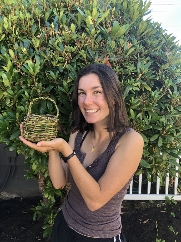 Woman holds up a basket she made from natural materials