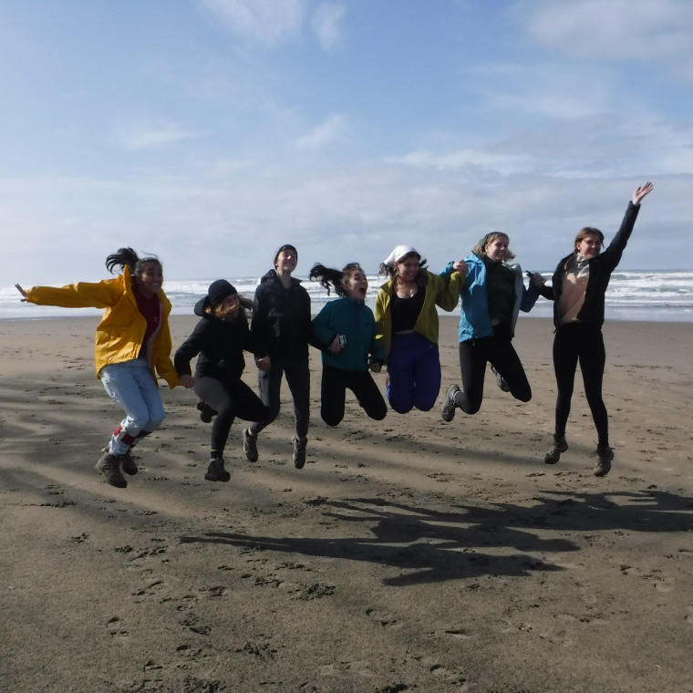 Participants jump in group on the coast with blue sky behind them.