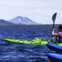 Image Description: Woman in a bright green kayak paddles on a blue lake with mountains in the background