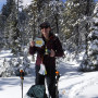 Participant poses with avalanche safety equipment with snow behind them.