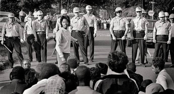 Sixteen-year-old Dorinda Palmer leads marchers to City Hall, blocked by white sheriff's deputies and local residents, including Ku Klux Klan members wearing street clothes. Greenwood, Mississippi, 1965.