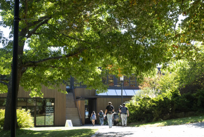 Exterior of building surrounded by tall trees and students walking on a path.