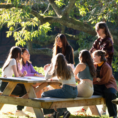Students sitting at tables on a green lawn.