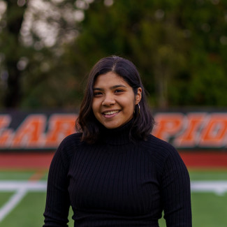 Ariely, in a black turtleneck, standing on the field at Griswold Stadium and smiling.