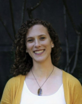 Stephanie is a Caucasian woman with long brown curly hair. She is wearing a yellow cardigan sweater with a white shirt.