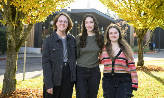 Three students smiling at the camera outside.