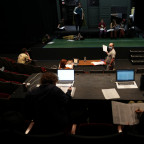 Theatre cast at a rehearsal, holding scripts on stage.