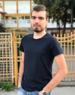Adin, standing in front of a yellow fence wearing a blue t-shirt and looking at the camera.