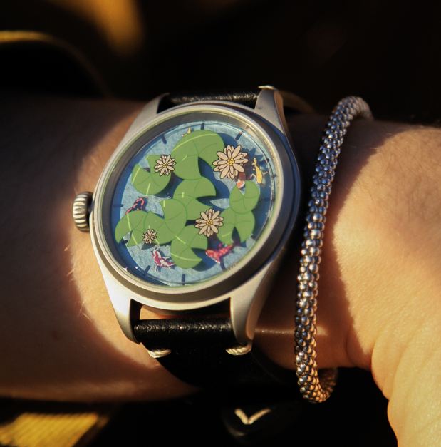 Close up of watch with a blue background, green lilypads, white flowers, and orange koi on the face.